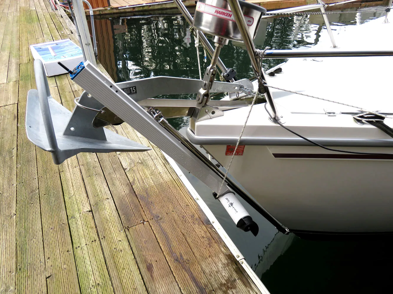 A DockStar on an aluminum track at the bow of a white sailboat moored at a wooden dock, beside a galvanized anchor, with its white pod down at the waterline and the propeller at its end.