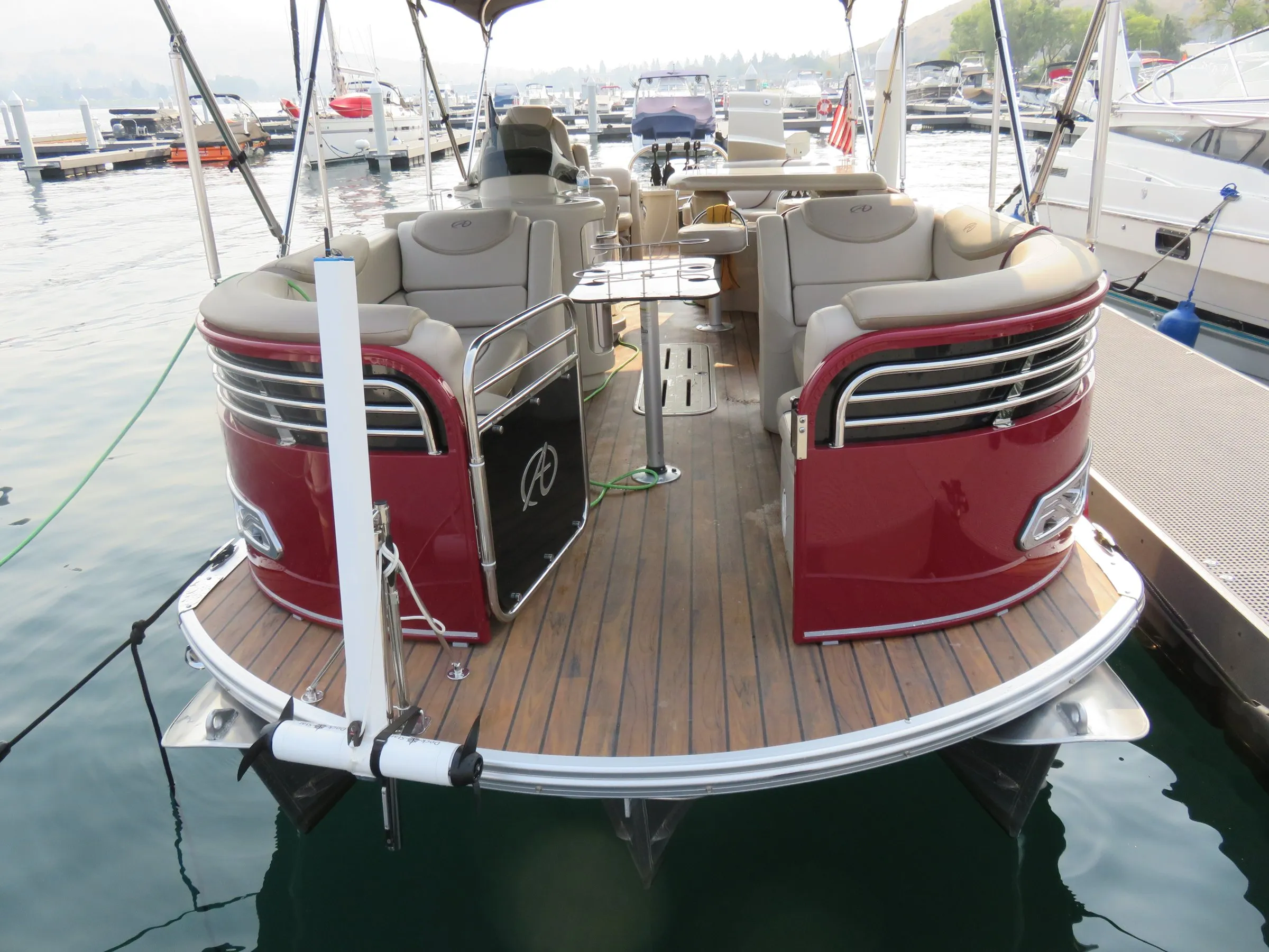 The deck of a red and cream pontoon boat tied in a marina, with a white DockStar mast on a track at the corner of the deck and its white pod and two black propellers raised just above the water.
