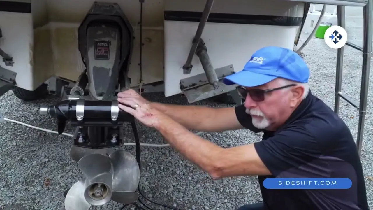A still from Sideshift's installation video: a man in a blue cap fitting the stern thruster to the sterndrive of a boat on its trailer.