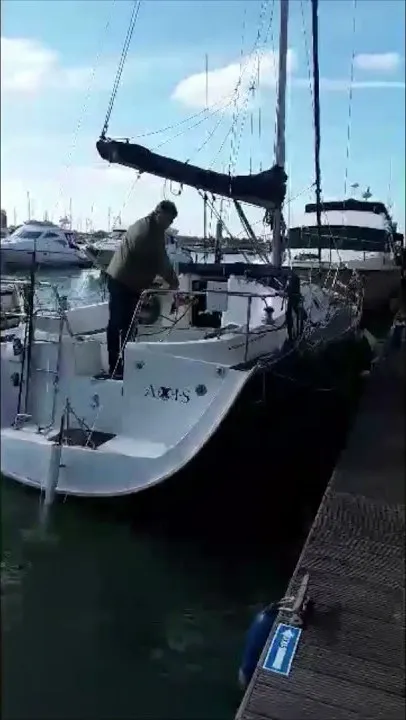 A still from DockStar's video, filmed upright on a phone: a man alone in the cockpit of a sailboat named Axis, coming alongside a floating dock.