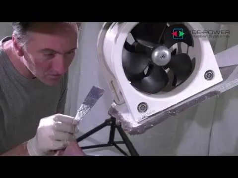 A still from Sleipner's retract installation guide: a man in gloves spreading sealant on the frame of a retractable thruster, its propeller facing the camera.